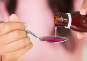 Woman hand pouring medication or antipyretic syrup from bottle to spoon. healthcare, people and medicine concept.